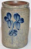 S559  Peter Herman Crock, This crock was made in Baltimore circa 1850 to 1870. It is decorated in cobalt with asingle stemmed,flowe. The crock has an attractive, smooth-sided shape , with the stamped signature about the flowers. a chip on the rim  10" tall