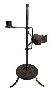 J402 18th century hand-forged wrought iron adjustable Combination Lamp featuring a Betty lamp and a candle holder on opposite sides of center post resting on a raised footed platform. The Betty Lamp / Whale / Fish Oil Lamp features sliding reservoir cover and internal wick support. The candle socket features fluted edge around the opening. Fantastic surface with evidence of hand forging and pitting indicative of age. Measurements: 5 ¼� diameter platform with overall height being 17� tall. (Raised platform is 2 7/8� tall)