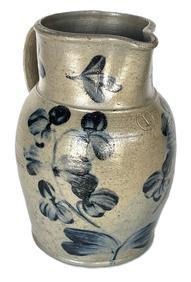 **SOLD** K271 19th century Baltimore, Maryland Peter Herman one gallon Crock Pitcher � stamped �I�. There is a small hairline crack in the rim. This small stoneware pitcher was made in Baltimore circa 1850 to 1870. It is decorated in cobalt with a two-stemmed flowering plant, along with flowers on the rim and highlights at the handle terminals.  Measurements: 10 &frac14;� tall. 