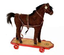 **SOLD** L133 Early 1900s Mohair Covered Pull-Toy Horse on wooden platform with wooden wheels. The solid wooden horse features hand carved and painted nose/mouth and hooves, glass eyes, mohair covering with natural horsehair mane and tail and leather tack with felt rosette decorations. The wooden platform retains original red painted border beneath a heavy patina and four original red painted wooden wheels that move freely. The horse is mortised into the base below each hoof. Original label remains intact on front of platform. Very good overall condition. Measurements: Base is 8 long x 2 ¾ wide. Height is ~8 ½ tall.