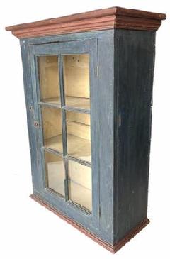  G906 19th century Pennsylvania original blue painted one door hanging cupboard featuring six wavy glass windowlites and red painted molding on top and bottom. Original oyster white painted interior. Square head nail and pegged construction. Measurements: The top is 27 1/2" wide x 12 1/4" deep. The case is: 24" wide x 10 1/4" deep. Overall height is 36 1/2" tall.
