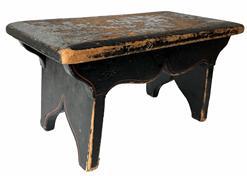 J152 Pennsylvania paint decorated wooden foot stool retaining original black painted surface with remnants of floral paint decoration on the top and simple pinstriping accents on the apron and each of the slightly splayed legs. The drop aprons on each side are mortised into the legs and boast a nice cut out that matches the cut out on each leg/foot. Chamfered edges along the top show extensive wear indicative of years of use. Square head nail construction. Circa 1840-1850s.  Measurements: 15 ¾ wide x 8 ¼ deep x 8 tall