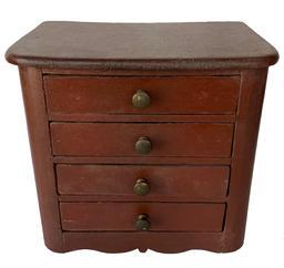 F105 Late 19th century miniature four drawer Chest in the original red paint. The top is one board with panel sides, a nice drop apron cut out base. The drawers are nailed construction with original knobs.