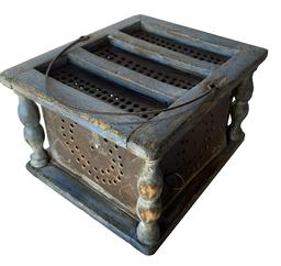 RM1319 1800s New England blue painted foot warmer/foot stove featuring nice corner turnings and the original sheet metal ember box boasting five punched heart shapes on each of the sides. The hand pierced circular holes on the sides and top allowed heat to be distributed evenly. The wooden frame is mortised and pegged construction. The ember box has nicely folded edges and the soldering is secure. Bale handle on top is secured with small early wire staple-type hooks. Door �hinges� and latch are comprised of early pieces of bent wire. Measurements: 9� long x 7 3/4� wide x 5 1/2� tall