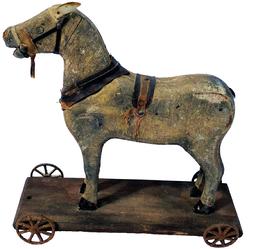 G533 Wooden Painted Horse Pull Toy on Wheels from the mid 1800s. There are still traces of the original saddle and harness . Original paint is worn, but there are traces of the old dapple-grey. Horse stands on the original shaped wood base with original cast iron wheels. Measures 10"high. 10"long. 4"wide.  