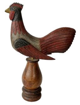 **SOLD** K160 Folk Art carved wooden Rooster mounted on tall turned wooden base for display purposes. Solid wood with detailed carved feathers and applied wings. Hand painted in red, gray, and black with a yellow beak and glass eyes.  Branded and signed by maker on bottom "Ken Kirby".  The wood is pine. Approximate measurements: 13 1/2" long x 3 1/4" wide x 18 1/2" tall  