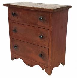 H1000 Excellent late 18th century New England miniature chest of drawers in original red painted surface featuring three graduated sized drawers with chamfered, solid wooden drawer bottoms resting on an exquisite cut out drop front apron and cut out ends.