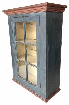 G906 19th century Pennsylvania original blue painted one door hanging cupboard featuring six wavy glass windowlites and red painted molding on top and bottom. Original oyster white painted interior. Square head nail and pegged construction. Measurements: The top is 27 1/2" wide x 12 1/4" deep. The case is: 24" wide x 10 1/4" deep. Overall height is 36 1/2" tall.