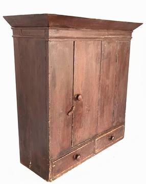 J252 Pennsylvania original red painted hanging cupboard with one door over two drawer configuration. Deeply canted applied molding around top. Combination of �T� and square head nail construction.  Great wear indicative of age and use. Circa 1790-1810. Measurements at top molding: 34� wide x 13 ½� deep. Case measures 30� wide x 11 ¼� deep. Overall height is 34 ¼� tall.