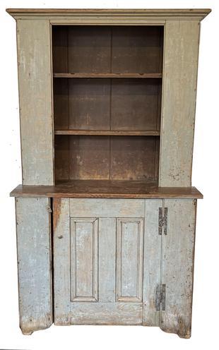 H408 American Country Stepback Cupboard. First half 19th century, pine. One piece with open top and paneled door in bottom with "H" hinges. Cut out feet, bead board back. Wrought iron nail construction. Cleaned down to gray with old brown paint on the inside. Worn with loss to feet and edges. Measurements: 72 1/2" tall x 43" wide x 17 3/4" deep