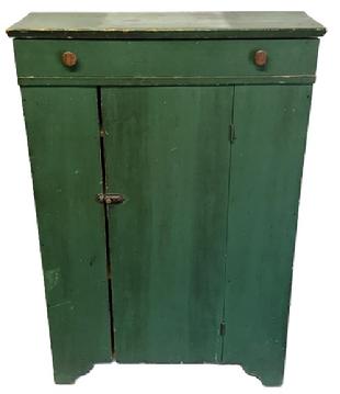 M1183 Wonderful 19th century Pennsylvania original green painted one door cupboard with full size dovetailed drawer above. Cupboard features a decorative cut out base, and the shaped overhang of the top is made to appear as a molded edge. Clean, natural patina interior with four stationery shelves. The wood is pine with square head nail construction. Circa 1850s-1860s. Measurements: 33 &frac12;� wide x 12 &frac14;� deep x 49� tall.  