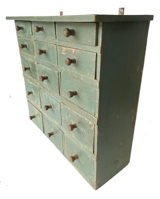 **SOLD** G864 19th century New England 15 drawer Apothecary.  Overhanging top above a bank of 15 graduated drawers, in rows of three, flanked by solid ends.  The drawer interiors display evidence of several color traces indicating it was possibly used to store different pigments. Retains likely original iron hanging straps and turned wooden knobs, and an early blue-painted surface. Mid 19th century. Measurements:  26 ½� wide x 10 ¼� deep x 24 ¾� tall