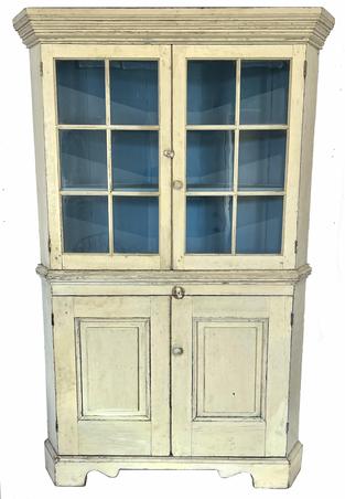 H299 19th century western Maryland white painted corner cupboard. One piece. Features two, six-pane glass doors over two raised panel doors below. All doors are fully mortised and pegged. Tall, applied bracket base with decorative cut outs. Wide, stacked cornice molding adorns the top and around the waist molding in center of the cupboard. Square head nail construction. The wood is white pine. Circa 1830�s. Measurements: 79� tall and takes a 26 ½� corner. 