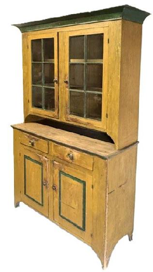 M318 Beautiful mid-19th century Lancaster County, Pennsylvania original mustard and green painted two-piece stepback cupboard boasting an unusual form with a high waisted base (40 &frac34;� tall). Applied wide cove cornice molding surrounds the top. The upper section has a cut-out pie shelf and two fully mortised 6-pane doors that open to reveal a clean painted interior with shelves and applied plate grooves/stops. The base boasts two dovetailed drawers over two, fully mortised raised panel doors that open to a clean interior with shelves for added storage. Stepback rests on tall cut out feet. The woods are pine and poplar with one-board, square head nail construction. Circa 1850s. Measurements: 61" wide at top (56 &frac14;� wide at waist) x 20 &frac12;� deep x 87" tall. 