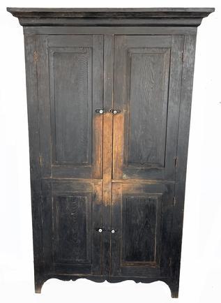 **SOLD** J106 Early 19th century Pennsylvania flat wall storage cupboard retaining its original black painted surface. The cupboard features four fully mortised and pegged raised panel doors, applied molding around top, tall feet with half-moon cut out ends and a beautiful decorative cut out apron on front.  Natural patina interior with upper interior shelves retaining applied wooden plate stops along the back of each shelf. Square head nail construction. Measurements: The top measures 47 ¾ wide x 18 ¾ deep. Case measures 42 wide x 16 deep. Overall height is 78 ¾ tall.