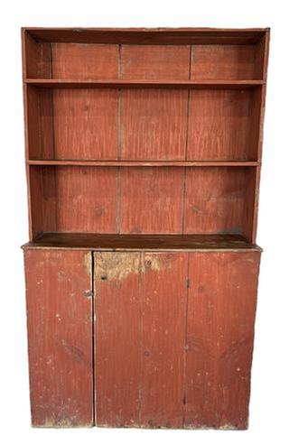 L56 Rare early 19th century New England Cantback Stepback Cupboard bearing original dry, bittersweet red painted surface. Each of the upper shelves bears a carved plate groove and the shelf fronts feature curved ends that cover where they are notched into the sides of the cupboard. The single door below opens to reveal an original blue painted interior. Batton on door boasts large rosehead nails. Circa 1800-1820s. Case is square head and wire nail construction. The wood is pine. Measurements: 43� wide x 17 &frac14;� deep (at waist) x 72 &frac34;� tall. 