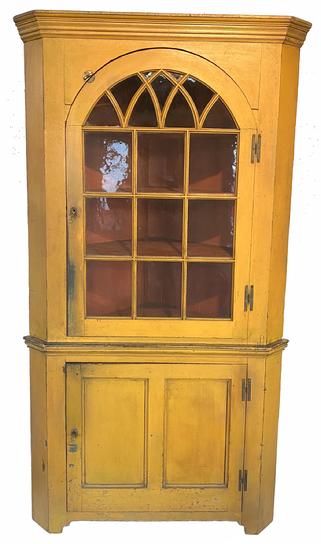 G863 BOLD LANASTER COUNTY, PENNSYLVANIA, VIBRANT YELLOW PAINTED PINE CORNER CUPBOARD. Two-piece construction, the upper section with applied complex-molded cornice over glazed door of arched profile, interior of the cupboard is a dry bittersweet red. Measurements: 87" H, 46" W, 33" corner. 
