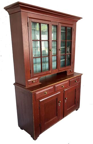 G443 Absolutely stunning early 19th century Lancaster Pennsylvania two-piece stepback Dutch cupboard in original red painted surface. The upper section boasts two, six-pane glass doors and a three-pane center column, two dovetailed candle drawers and a tall cut out pie shelf. Upper doors open to a clean, pale blue painted interior with shelves that have both plate grooves AND removable plate rails with nicely beaded edges. The bottom of the cupboard features three dovetailed drawers over two doors and rests on short applied turned feet. Lower doors open to reveal shelves and a clean, natural patina interior. All doors are fully mortised and wooden pegged. All doors and drawers feature chamfered edges on their fronts. Applied molding around top, and along edges where top rests on base. Handwritten information identifies this cupboard to a family in Lancaster, Pennsylvania. (Please see photos for additional details.) Original brass hardware remains intact. Square head nail construction. Circa 1830-1840s. Measurements: 59 ¼� wide x 19 ¾� deep x 81 ½� tall