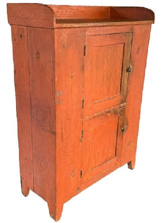 L131 Beautiful early 19th century Pennsylvania original bittersweet red painted jelly / storage cupboard featuring an unusual door over door configuration with applied dovetailed gallery, resting on cut out feet. The panel doors are mortised and wooden pegged construction. Case is square head nail construction. Clean, natural patina interior with shelving for added storage options. The wood is pine. Circa 1830s. Measurements: 41 ¾ wide x 18 ¾ deep x 58 ¾ tall (back) x 54 ¾ tall (front).