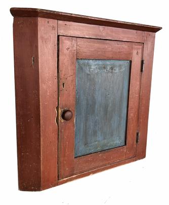 H121 Early 19th century Pennsylvania hanging Corner Cupboard, in the original red and blue paint. This Cupboard has a single  panel door which is mortised and pegged, that open to the interior that is also has the original blue paint, it is one board square head nail  construction  25" high , 29" wide .