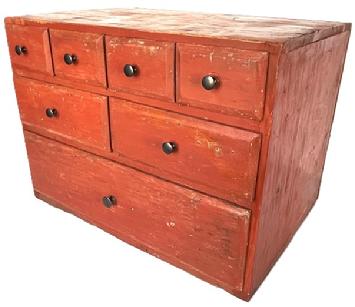 **SOLD** K1602B Early 19th century Pennsylvania original red painted apothecary featuring dovetailed case and seven dovetailed drawers. Unusual configuration of four, over two, over one drawer layout. Drawer stretchers are mortised into the case and each of the drawer fronts have chamfered edges. Square head nail and dovetail construction. The wood is pine. Circa 1820s. Measurements: 22 ¼ wide x 15 ¼ deep x 16 ¼ tall.  