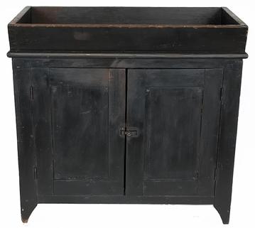 J82 Beautiful 19th century original black painted dry sink with canted dovetailed well over two fully mortised panel doors. Solid ends with a nice, high cut-out foot. The back boards are held in place with square head nails.  Clean, natural patina interior with shelves for storage. Square head nail construction. Great wear to inside of well from years of use!  Circa 1820.  Measurements: 19 1/2" deep x 36" wide x 33 3/4" tall