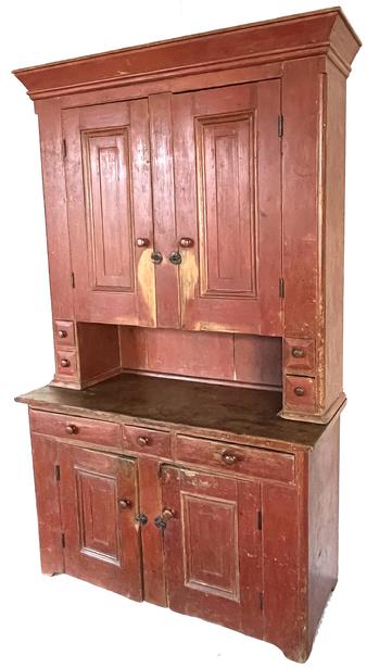 J431 Spectacular early 19th century Pennsylvania two-piece original red painted stepback cupboard boasting a host of aesthetically appealing attributes including a wide, flared cornice molding surrounding the top, ¼ round molded corners, stepped molded panel doors, a tall, recessed pie shelf and cut out feet. The unusual configuration consists of two upper doors with two beveled edge spice / candle drawers on each side of the unusually tall, recessed pie shelf which creates a great work surface. The top rests on a base that has three beveled edge drawers above two doors that open to a clean, natural patina interior. The interior of the top retains an original green painted surface with wear indicative of years of use. All doors are fully mortised and are surrounded by beaded edges. Circa 1820s � 1840s. Measurements: 52 ½� wide (top) x 19 ¾� deep (waist) x 84� tall