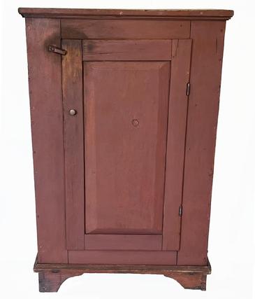 J288 Wonderful early 19th century Pennsylvania one door cupboard in original red painted surface featuring an oversized dovetailed base with cut out feet, applied moldings and a beautiful, raised panel door that is mortised and pegged. Clean interior with sturdy shelves for storage. Square head nail construction. Circa 1810s-1820s. Measurements: 34� wide x 16 ¼� deep x 51� tall. 