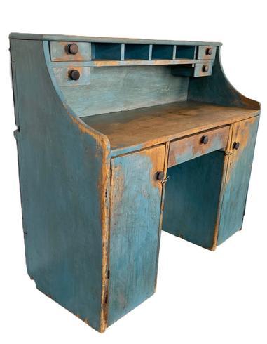 K274 Unusual 19th century Pennsylvania Merchant's Desk with unique hidden hinged drop-down writing surface in old blue painted surface. Desk boasts drawers and pigeonholes in the top section for added storage. The top board is hinged so that it can be raised to utilize the top row pigeonholes for sorting taller items. The lower section, known as a kneehole style, boasts two doors and a center drawer.  This versatile piece could be used against a wall � or it could be shared by two parties simultaneously as a Partner�s Desk. Wire nailed construction. Circa 1870s. Measurements:  47 &frac14;� wide x 20� deep x 41 &frac34;� tall (back) x 2/ &frac12;� tall (front).  
