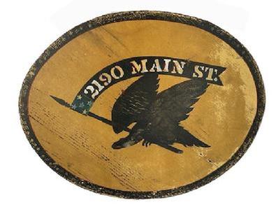 K1834 Double sided wooden sign with an Eagle holding a flag/banner in its beak that reads �2190 Main Street�. Painted in black with polychrome accents on a mustard yellow colored background. Black border detail around the outside edges adds nice appeal. Old eye hooks remain intact on top and wire has been added for hanging purposes. Weathered surfaces indicate years of use in an outdoor setting. Measurements: 21 &frac12;� wide x &frac34;� thick x 17 &frac14;� tall. 