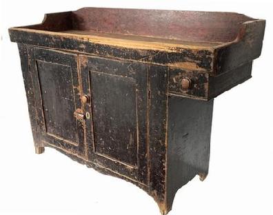 J168 19th century York County, Pennsylvania painted pine dry sink with overhanging drawer retaining original black painted surface. Delicately scalloped cut out apron adorns the front. The well boasts shaped ends and the interior of the well retains remnants of old red paint and bears extensive wear from years of use. Drawer is dovetailed. Doors are fully mortised with nicely beaded edges. Square nail construction. Circa 1820s. Measurements: 50 ¾ wide x 19 deep x 36 tall (back) x 32 ¼ tall (front)