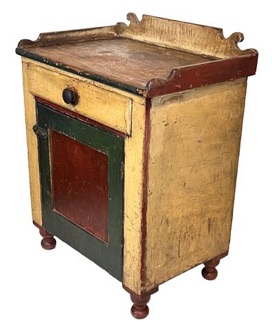 H110 Lancaster County, Pennsylvania one drawer wash stand in original red, green and yellow paint.  This great piece features a dovetailed applied decorative cut out gallery, applied turned feet and a single dovetailed drawer with divided interior over one door that is fully mortised and pegged. Clean interior with interior shelf for storage. Square nail construction.  Measurements: 27 1/2" wide x 19" deep x 35 3/4" tall (back)