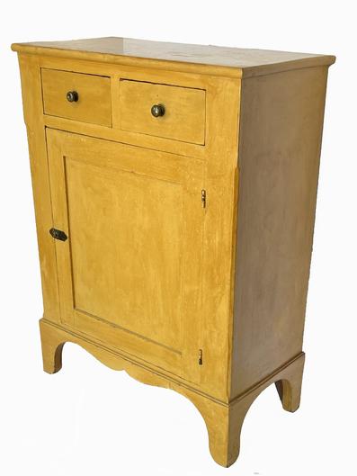 H937 Exceptionally nice early 19th century Pennsylvania original yellow painted one door storage cupboard with two dovetailed drawers over one mortised and pegged door resting on a tall, applied bracket base featuring high cut out feet and a drop double scallop cut out apron.  Chamfered corners on front add to the list of fine details in the workmanship of this piece. Squarehead nail construction. Super clean, natural patina interior with shelves for storage. Circa 1820�s. Measurements: 28 ¾� wide x 14 ¼� deep x 38 ¼� tall (7 ½� tall base)