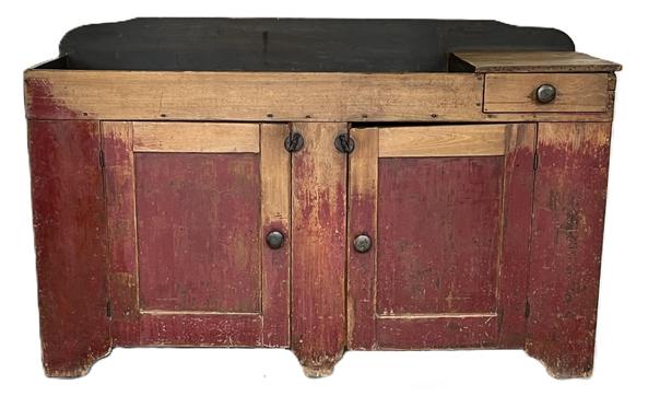 K1723 19th century Pennsylvania original red painted drysink with remnants of blue paint inside the well. One dovetailed drawer. Two doors below the well open to reveal shelf for additional storage. Very unusual long form with center foot to help support the weight. The wood is pine. Great wear on front from years of use. Circa 1850s. Measurements: 60 wide x 21 deep x 35 ¼ tall (back)