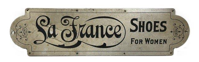 M1153 Early 20th century Trade sign advertising �La France Shoes For Women�. Metal front on a wooden framed back. La France Shoe Company was established in Lynn, Massachusetts in the early 20th century and became a national brand that was iconic between 1900 and the 1920s for their elegant, tailored women�s shoes with �comfort arch�. Measurements: 30� wide x &frac12;� thick x 8� tall.  